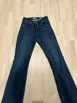 Bootcut jeans från Wrangler - Mörkblå bootcut jeans från Wrangler med klassisk femficksdesign och snygga kontrastsömmar. Jeansen har en något utsvängd passform nedtill och är tillverkade i ett slitstarkt denimtyg. Perfekta för en avslappnad och trendig look.
