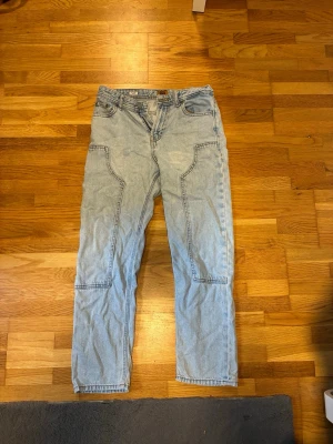 Ljusblå loose fit jeans med kontrastsömmar - Säljer ett par ljusblå jeans i loose fit-modell med stora fickor fram och bak. Klassisk femficksdesign och raka ben. Perfekta för en avslappnad och trendig look. Materialet är denim i bomull.