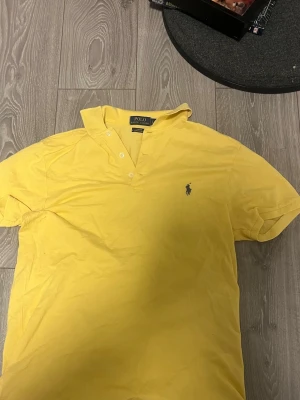 Gul pikétröja från Ralph Lauren - Snygg gul pikétröja från Polo Ralph Lauren i slim fit med klassisk krage och knappar framtill. Tröjan har det ikoniska broderade logotypen på bröstet och är tillverkad i stretchigt bomullsmaterial som ger en bekväm passform. Passform är M/L