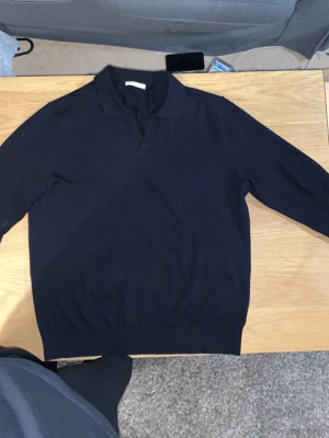 L. Zara Mörkblå pikétröja med lång ärm - Har haft den i 1 månad bara inga hål eller problem med tröjan Max har haft den på mig 5 gånger Snygg marinblå långärmad pikétröja med klassisk krage och v-ringad öppning. Tröjan har en enkel och stilren design, perfekt för dig som gillar en clean look. Tillverkad i mjukt material som känns skönt mot huden.