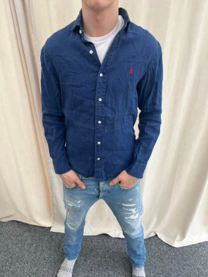 Marinblå skjorta från Ralph Lauren - Snygg marinblå skjorta från Ralph Lauren med klassisk krage och knappar framtill. Strl S, personen på bilden är 183 cm lång. Skicka gärna prisförslag. Kika in min profil för mer schyssta plagg