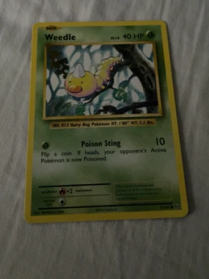 Weedle Pokémonkort Base Set - Säljer ett klassiskt Weedle Pokémonkort från Base Set. Kortet har grön ram, gul kant och motiv av Weedle i en tecknad skogsmiljö. Text och detaljer på engelska. Perfekt för samlare eller Pokémonfans!