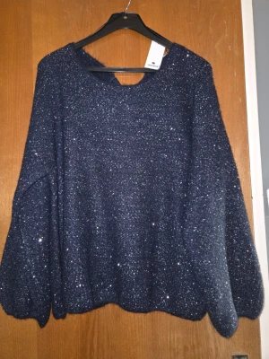 Mörkblå glittrig stickad tröja - Mysig stickad tröja i mörkblått med glittriga inslag. Tröjan har rund halsringning, ballongärmar och ribbade muddar. Perfekt för dig som vill ha något extra till din outfit. Materialet känns mjukt och stretchigt.