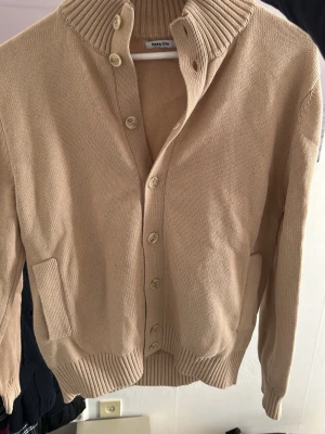 Kofta med knappar - Stilren beige kofta från Tour & Tate med hög krage och knappar. Säljer den för jag inte använder den längre. Storlek small tror jag men den passar också medium. Säljs för 299kr. Kontakta mig om du har frågor.
