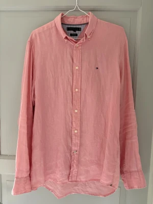 Rosa skjorta från Tommy Hilfiger - Säljer en klassisk rosa skjorta från Tommy Hilfiger med button-down krage och små vita knappar. och den ikoniska Hilfiger-loggan broderad på bröstet. Tillverkad i mjuk bomull för en skön känsla.