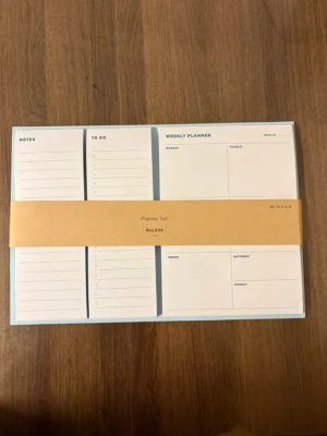 Planner Set från Åhléns, blå - Snyggt och praktiskt planner set från Åhléns i ljusblått med beige band. Innehåller sektioner för anteckningar, att-göra-lista och veckoplanering. Perfekt för att hålla koll på veckan och organisera vardagen. Tillverkad i papper.