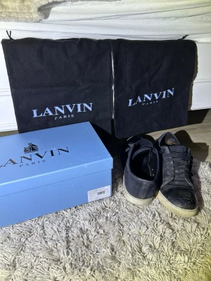Lanvin mörkblåa/svarta låga sneakers - Snygga mörkblåa/svarta sneakers från Lanvin i mocka och läderdetaljer. Skorna har vita sulor och klassisk snörning. Kommer med originalkartong och dustbags. Perfekta för dig som vill ha en stilren och exklusiv sneaker i garderoben. Skorna är även signerade av så kallad ”Skoovby” men vill man inte ha det så går det bort på 30 sekunder. De är fult äkta med box och dustbag,säljer billigare pga kvitto inte finns.
