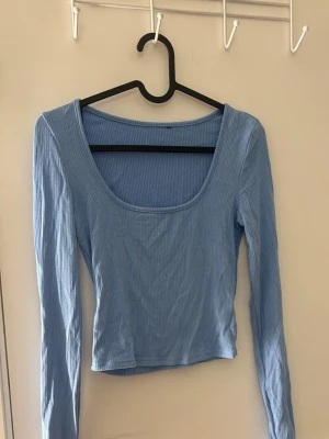 Ljusblå ribbad långärmad topp - Trendig ljusblå långärmad topp med ribbad struktur och djup, rundad urringning. Croppad modell som passar perfekt till höga jeans eller kjol. Enkel och stilren design som är lätt att matcha.