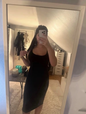 Svart ärmlös klänning med smala axelband - En stilren svart klänning med smala axelband och figurnära passform. Klänningen är ärmlös och har en klassisk, enkel design som slutar strax under knäet. Perfekt för dig som gillar minimalistisk stil. Jätte bra skick