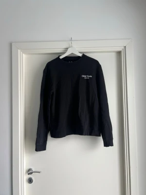 Svart långärmad tröja Cheap Monday - En svart sweatshirt / sweater / pullover / crewneck från Cheap Monday med rund halsringning och lång ärm. Diskret logga i vitt på bröstet. Tillverkad i mjukt bomullsmaterial som är skönt att ha på sig. Enkel och stilren design som passar till det mesta. Storlek S / small. Måtten finns. 