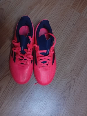 Adidas fotbollsskor  - Säljer ett par snygga fotbollsskor från Adidas med klassiska svarta ränder på sidorna. Skorna har snörning och en låg profil, perfekta för snabba rörelser på planen. Ovandelen är i syntetmaterial och insidan är mörkblå.