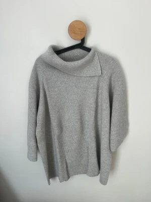 Ljusgrå trekvartsärmad stickad tröja från COS - Säljer en ljusgrå stickad tröja från COS med bred polokrage och avslappnad passform. Tröjan är ribbstickad och har trekvartsärmar. Tröjan är i super fint skick! Hör av dig vid frågor och funderingar! 