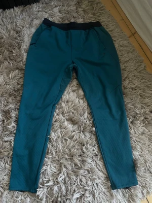 Turkosa mjukisbyxor från Gymshark - Snygga turkosa mjukisbyxor från Gymshark med svart resår i midjan och två sidofickor. Byxorna har en smal passform och är tillverkade i ett mjukt, strukturerat material som känns skönt mot huden. Perfekta för chill eller träning.