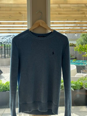 Ljusblå stickad tröja från Polo Ralph Lauren - Snygg ljusblå stickad tröja från Polo Ralph Lauren med rund halsringning och diskret broderad logga på bröstet. Tröjan har långa ärmar och ribbade muddar vid ärmslut och nederkant. Perfekt för en stilren och avslappnad look.