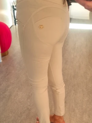 Beige skinny byxor från Freddy W.R  - Snygga beige skinny jeans från Freddy W.R Up med guldfärgad logodetalj på bakfickan. Byxorna har klassisk femficksdesign och stretchigt material som sitter tight och bekvämt. Perfekt för dig som gillar stilrena och moderna byxor.