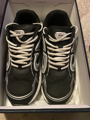 Svarta snygga sneakers - Snygga svarta sneakers med vita och grå detaljer samt vita skosnören. Ovandelen är i mesh och läder för en sportig och exklusiv look. Tjock vit sula ger extra streetkänsla och komfort. Perfekta för dig som vill sticka ut med ett par lyxiga sneakers.