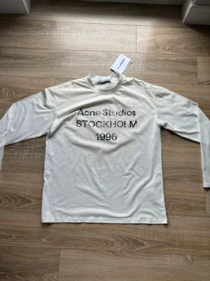 Vit långärmad t-shirt Acne Studios - Helt ny långärmad t-shirt från Acne Studios. Klassisk rund hals och relaxed fit. Tillverkad i mjuk bomull som känns skön mot huden. Perfekt för dig som gillar stilrena och trendiga plagg.