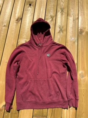 Vinröd hoodie - Snygg vinröd hoodie. Klassisk magficka framtill och en liten rund patch på bröstet. Tillverkad i mjukt sweatshirtmaterial som känns skönt mot huden. Perfekt för en avslappnad och trendig look.