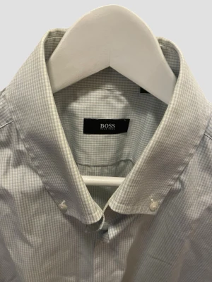 Blåvit kortärmad skjorta från BOSS (44) - Snygg kortärmad skjorta från BOSS i diskret blåvitt randigt mönster. Klassisk krage och knäppning framtill. Perfekt för en stilren look och tillverkad i bomull för en skön känsla. Storlek 44. Passform: slimfit. Alternativ gå upp en storlek om du normalt sätt t ex har 43. 