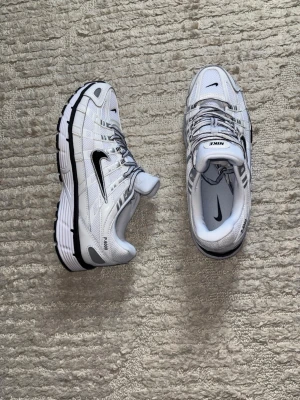 Nike P-6000 vita sneakers - Nike P-6000 sneakers i vitt mesh och syntet med svarta detaljer och silvriga inslag. Skorna har en chunky sula med svart och vit yttersula, samt klassisk Nike Swoosh på sidan. Perfekta för en sportig och trendig look.