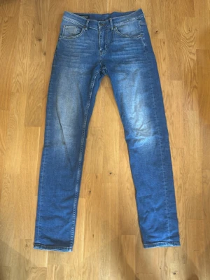 Blå slim fit jeans från J. Lindeberg - Snygga blå slim fit jeans från J. Lindeberg med klassisk femficksdesign och snygga slitningar framtill. Jeansen har normal midja och är tillverkade i mjukt denimtyg som ger en bekväm känsla och stilren look.