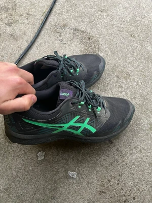 Asics GEL-FUJISETSU 3 GTX M - Säljer ett par svarta Asics löparskor med gröna detaljer och mönstrad sula med metallpiggar för extra grepp. Skorna har snörning och är tillverkade i slitstarkt syntetmaterial och mesh för bra ventilation. Perfekta för terränglöpning och orientering. Är i goretex och har broddar. Nypris 1799