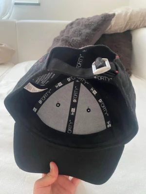 Svart New Era 9FORTY keps - Snygg svart keps från New Era, modell 9FORTY. Justerbar rem baktill med metallspänne för perfekt passform. Klassisk böjd skärm och ventilerande hål upptill. Tillverkad i bomullsmaterial för en bekväm känsla.