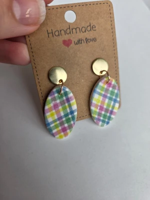 Handgjorda rutiga örhängen - Färgglada handgjorda örhängen med ovala hängen i rutigt mönster i blått, gult, rosa och grönt. Överdelen är en rund, guldfärgad platta. Perfekta för dig som gillar unika accessoarer med retrovibbar. Gjorda för hand av mig i polymerlera. 