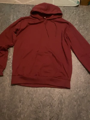 Vinröd hoodie med huva från arket - En enkel och stilren vinröd hoodie med huva och dragsnören. Hoodien har en klassisk känguruficka framtill och ribbade muddar vid ärmslut och nederkant. Perfekt för dig som gillar en clean look. Materialet känns mjukt och bekvämt, troligen bomull eller bomullsblandning.