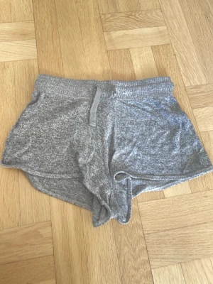Grå mjuka shorts med snörning - Mysiga grå shorts i mjukt material med snörning i midjan. Perfekta för lata dagar hemma eller till träningen. De har en loose passform och elastisk midja för extra komfort.