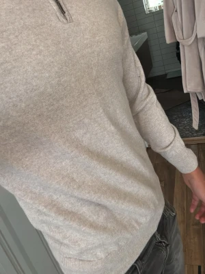 Half zip Berkley cahsmere - Snygg beige cashmere stickad tröja från Berkley med halvzip och ribbade muddar. Tröjan har en klassisk passform och är tillverkad i mjukt material som känns skönt mot huden. Perfekt till jeans eller chinos för en clean look.
