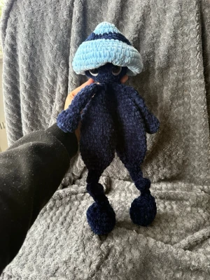 Blå virkad svamp - Unik handgjord svamp i mörkblått och ljusblått garn. Den har stora broderade ögon, långa armar och ben samt en fluffig, rundad huvudform. Perfekt som dekoration eller gosedjur för dig som gillar söta och annorlunda figurer.