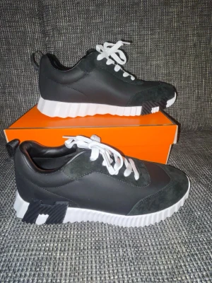 Svarta H sneakers med vit sula - Snygga svarta sneakers med vit, räfflad platåsula och vita skosnören. Ovandelen är i en mix av mocka och slätt material. Sulan har svarta detaljer undertill och cool design. Perfekta för dig som vill sticka ut med din stil.