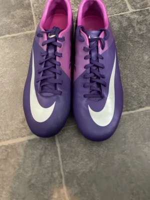 Nike mercurial vapor superfly - Säljer ett par klassiska snygga fotbollsskor från Nike i lila och rosa med stora vita swoosh-loggor. Skorna har klassisk snörning och metall-dobbar för bra grepp på planen. Tillverkade i syntetmaterial som ger en tight och bekväm passform. Perfekta för dig som vill sticka ut på matchen!