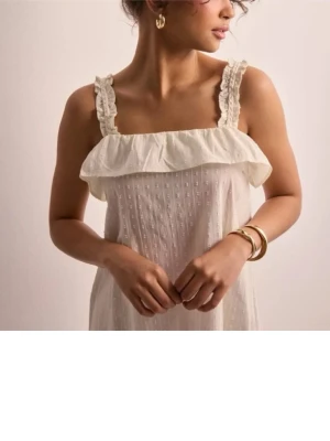  långklänning med volang - Offwhite långklänning med breda axelband och volangdetalj över bysten. Klänningen har ett diskret prickigt mönster och är ärmlös. Tillverkad i ett lätt och luftigt material som ger en avslappnad känsla.