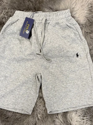 Grå shorts från Polo Ralph Lauren - Melerade grå sweatshorts från Polo Ralph Lauren med klassisk broderad logga på benet. Shortsen har elastisk midja med snörning och två sidofickor. Perfekta för chill dagar och har en avslappnad passform.