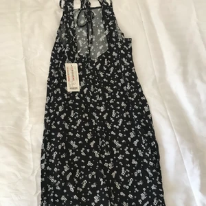 Svart klänning med vita små blommor - Helt ny svart klänning med små blommor. Jättemjukt och skönt material. Linneklänning med knytning i bak, kan även knytas bakom och sedan runt midjan för att få fram formerna. Strl XS, aldrig använd, passar även S. Nypris 149kr😇