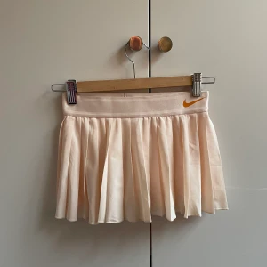 Nike Mini tennis kjol - Säljer en sån här så trendig Nike tennis kjol som är i barn storlek men passar såå snyggt som en mini kjol!! Ändvänd få gånger, i så bra skick är i en ljusrosa/beige färg, sjukt snygg!! OBS! Utrops priset är 150 inte 200