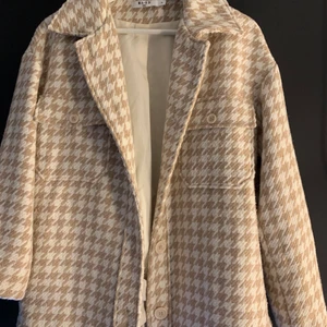 Jacka - Jacka från Na-kd i ett rutigt mönster i beige och vitt. Storlek 34, oversized. En tjock variant av skjortjacka vilket gör att den är perfekt för höst/tidig vinter-väder. Material: 70% polyester, 30% ull. Väldigt fint skick🤍