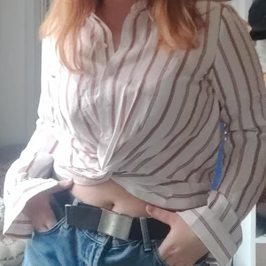 Crop Top Skjorta från New Yorker - Stilig och diskret crop tip - skjorta från New Yorker med röda och svarta ränder! Köptes sommaren 2020 och är i princip oanvänd. Skjortans framsida ger en snygg illusion av en knut som gör att den blir som en crop top. I bak är det en elastisk resor. Köptes på New Yorker för 149kr.