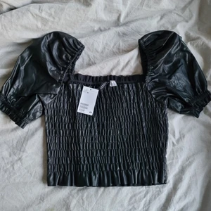 Tank topp i ”skinn” - En svart tank top i ”skinn/läder”, den är endast provad men den var för stor för mig men i gått skick, köpte den för ungefär en månad sen. Den har puffärmar och är ribbad❣️tvättas innan jag skickar den🖤