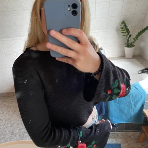 Svart stickad magtröja - Fin svart stickad magtröja med utsvängda ärmar och blommor broderade på båda ärmarna. (Se tredje bilden) Nästan aldrig använd och är då i nyskick utan skador. 