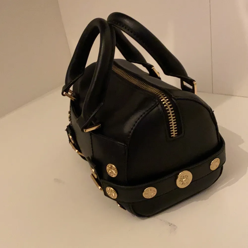 En mindre svart bowler väska med guld detaljer från Topshop. Det finns ett ytterfack, samt en korthållare i huvudfacket. Är i topp skick! B:14L:20H:14 (cm). Laukut & Käsilaukut.