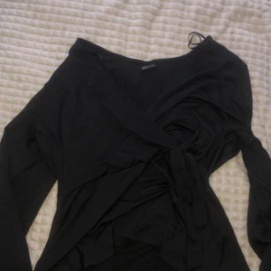 Tröja  - En svart mer uppklädd tröja med knytning vid midjan. Den har lite utsvängda armar vid vristen. 