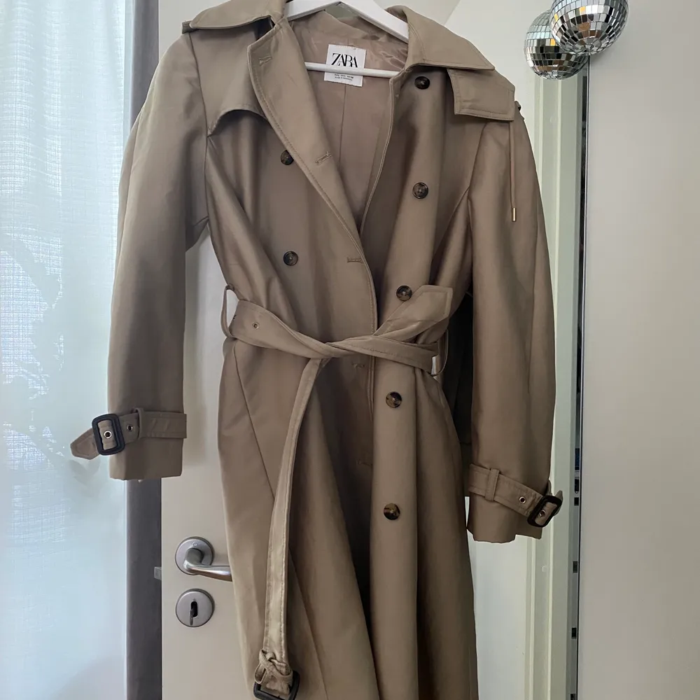 Rejäl och snygg trenchcoat från Zara i strl L (mer som S-M). Väldigt fint skick, men har dock några svarta streck på knytningen (bara skriva om ni vill se bild). Annars i fint skick. Trenchcoaten har en luva, men den går att ta av. På första bilden bärs den av en xs-s o på andra en M. Säljs för 266kr inkl frakt🤍🤍. Jackor.