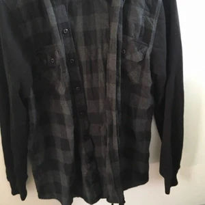 Flannel luvtröja - En flannel luvtröja med svarta ärmar och luva i samma material som hoodies brukar vara! Svarta knappar för att stänga den och två användbara fickor på bröstet med en knapp var. 150kr men går att diskutera!