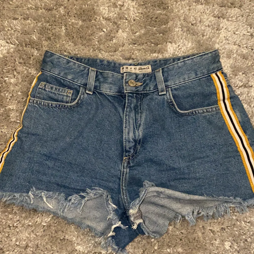 Mörkblåa jeansshorts från Primark med en gul, svart och vit kant på båda sidorna. Modellen är 160.. Shorts.