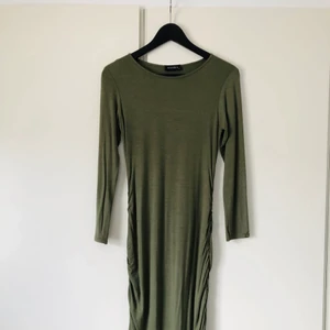 Mörkgrön figurnära klänning - Mörkgrön figurnära klänning med smock på sidorna från CLUB L. 