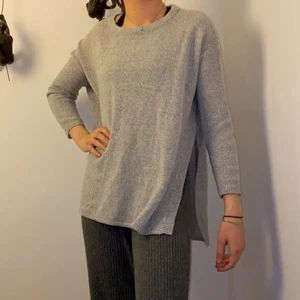 Stickad tröja  - Stilren och modern stickad tröja, i en ljusgrå färg! Tröjan har en cool slit på båda sidor och den bakre delen är lite längre! Storlek XS/S! 