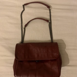 Väska - En superfin vinröd väska i läderimitation från Zara. Den är använd ett fåtal gånger och är därför i ett fint skick.  Det är en lång kedja på väskan så man kan antingen välja om man vill ha den som crossbody eller vid axeln